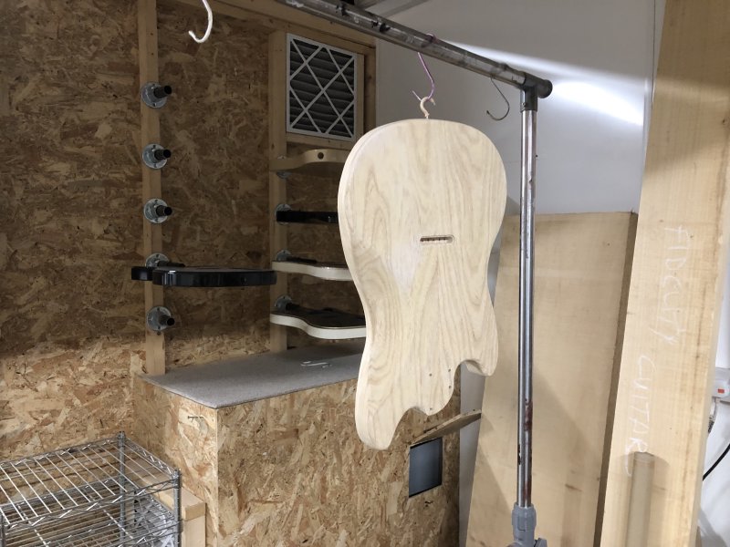 The guitar body is hung up on a rack using a hook attached where the lower buttons strap will go. You can kinda see that  the surface is a bit blotchy, a result of applying the grain filler and not yet having sanded it back.