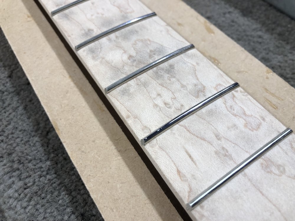 A close up on some frets after the first sanding pass. Most frets have shiny metal showing all the way across, but one of them still has black sharpie on it for about 20% of its length. The fretboard looks a little grubby now as sharpie/metal dust has been sanded onto it.