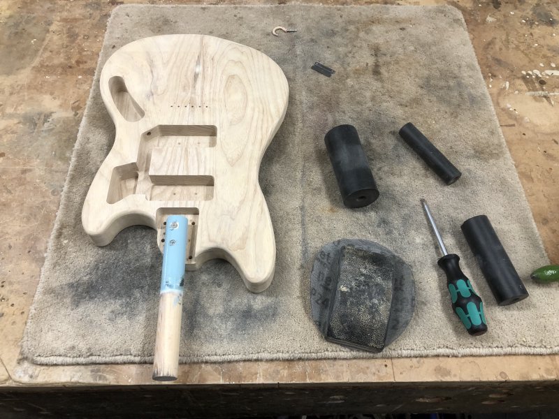 The guitar body now sits on the workbench with a short wooden baton, about a foot long, stuck where the neck would go on the finished guitar.