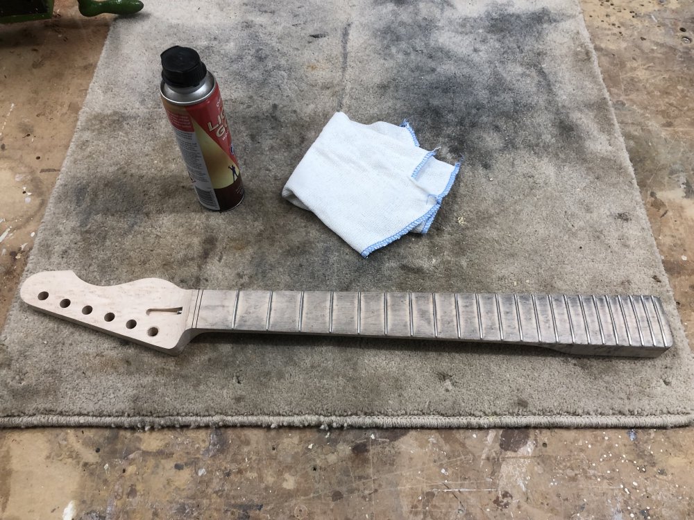 The neck again, but now the fretboard is covered in a gray dust, looking quite dirty. Beside it sits a can of 'liquid gold' cleaning fluid and a clean cloth.