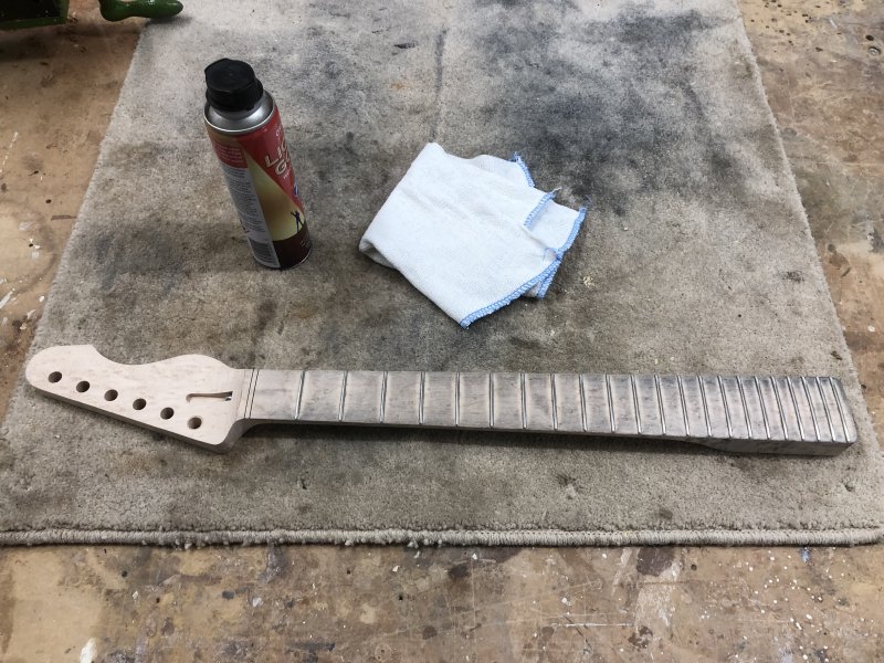 The neck again, but now the fretboard is covered in a gray dust, looking quite dirty. Beside it sits a can of 'liquid gold' cleaning fluid and a clean cloth.