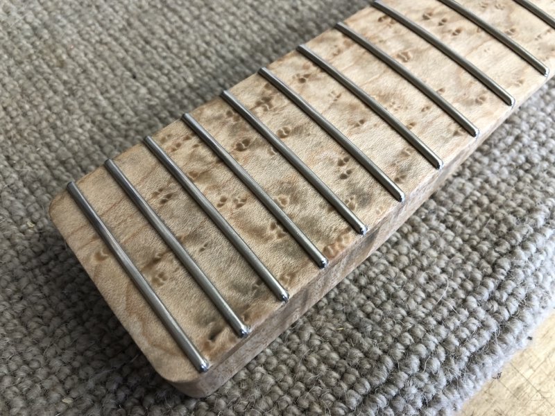 A close up of the fretboard, which looks darker now because it's wet with the cleaning fluid, but there's notable darker splodges that are more grey than gold as you'd expect from figured wood. It does not look nice.