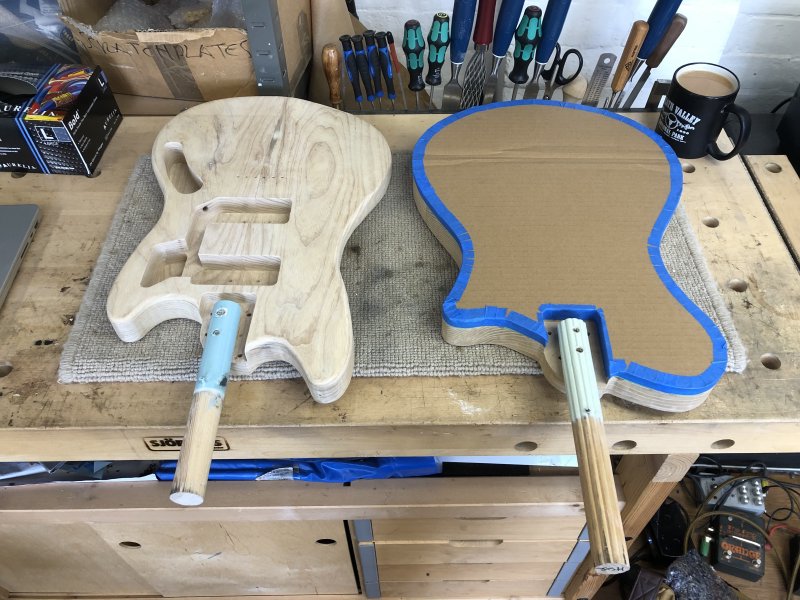 Two guitar bodies sit on the workbench, and both have a short wooden poll attached into the neck pocket.