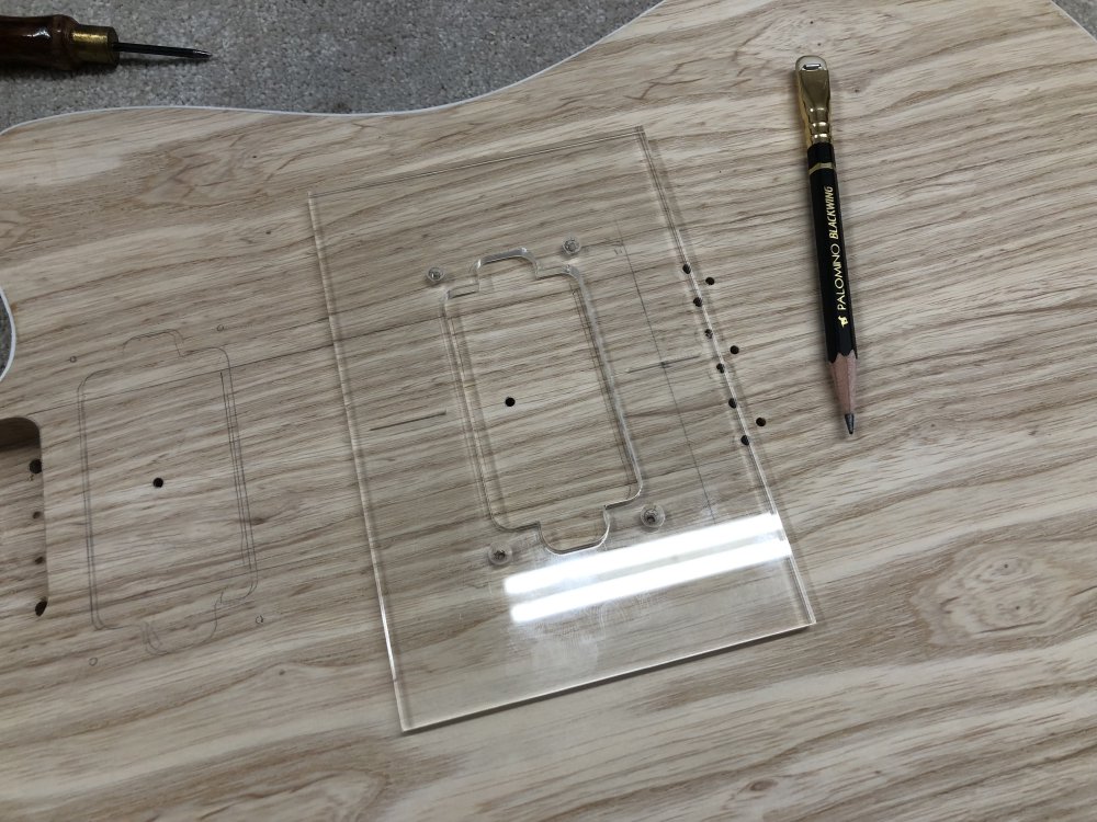 A close up on the front of the guitar body showing a clear acrylic routing template has been placed where one of the pickups needs to go.