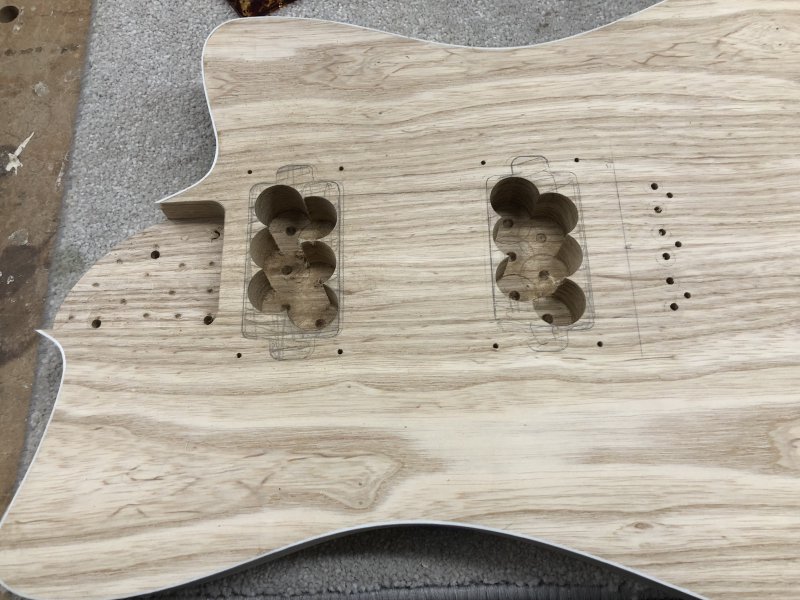 The guitar body sits on the workbench again, now where the pickup cavities are there are six interlined holes drilled to a depth of about 25mm in each of the hatched areas that marks where the two pickups will go.