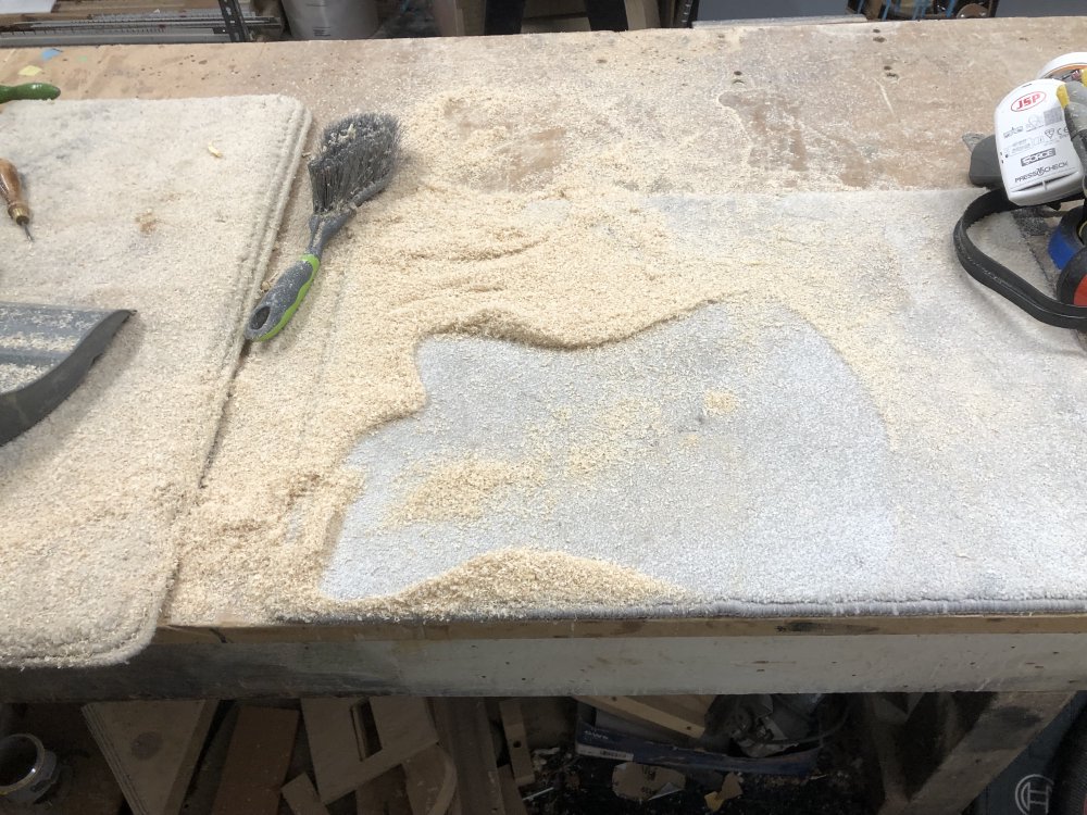 The workbench with the guitar body removed, leaving a clean silhouette in a sea of wood dust otherwise covering the workbench.