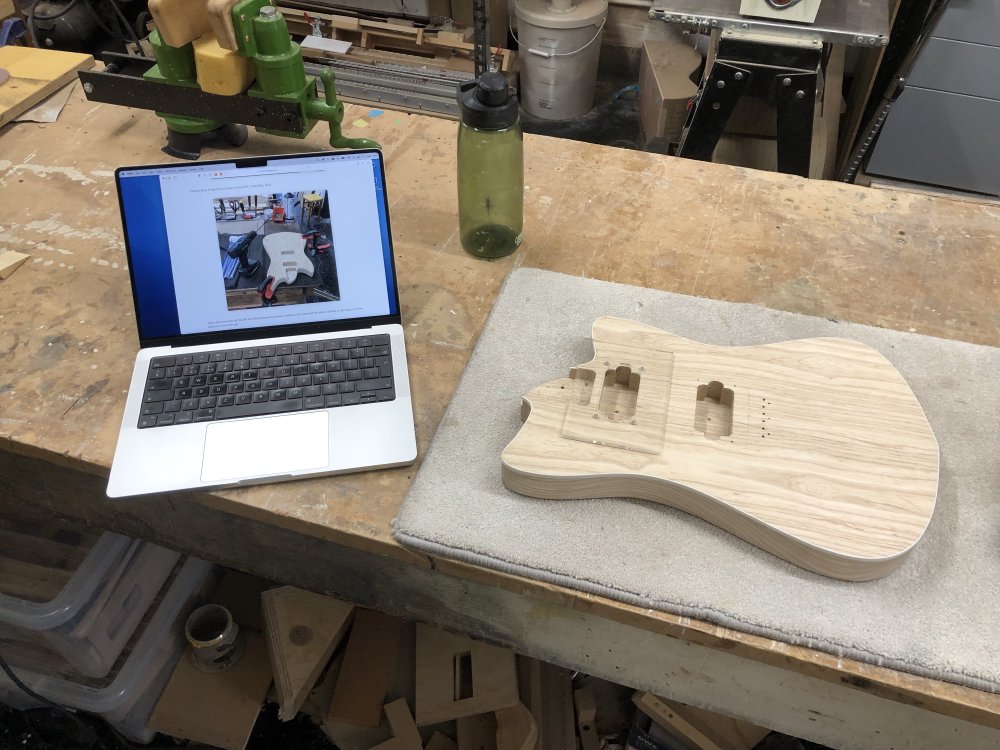 The guitar body sits on the workbench, and next to it is my laptop, and you can see a browser is open with a picture of a guitar body being worked on.