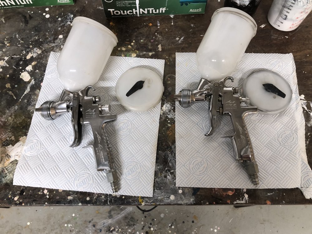 Two chrome metal spray-guns with plastic paint cylinders on top rest open on the workbench.