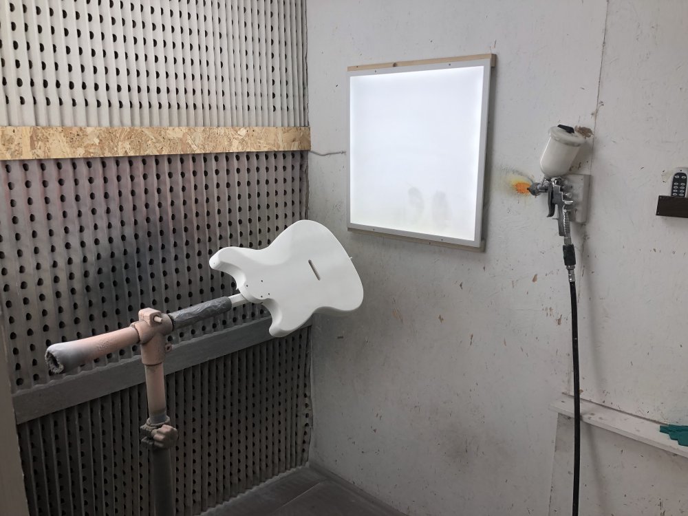 The body of Hästen sits mounted in clamp at chest height in the spray-booth, next to a light panel, and on the wall is hung the spray-gun with white primer in it connected to the air-hose.