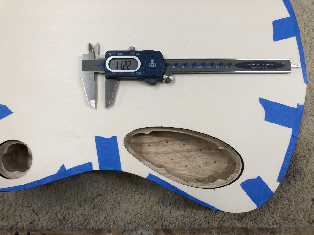 A top down shot of the template mounted on the guitar, so you can see the electronics cavities and the lip area that needs to be cut. On top of the template is a set of digital callipers reading 11.22 mm