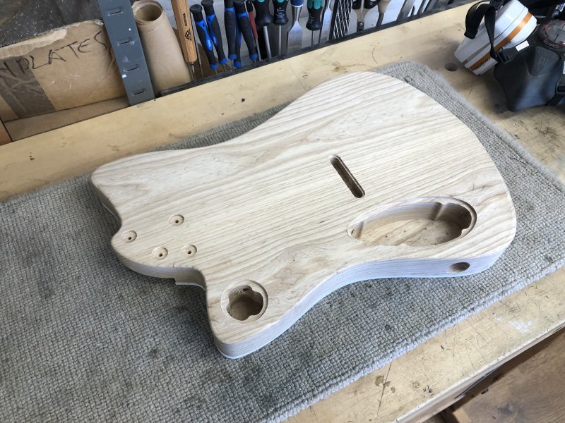 The guitar body sits on the workbench face down, showing the electronics cavities and the lips around the edge of each one where the cover will be mounted.