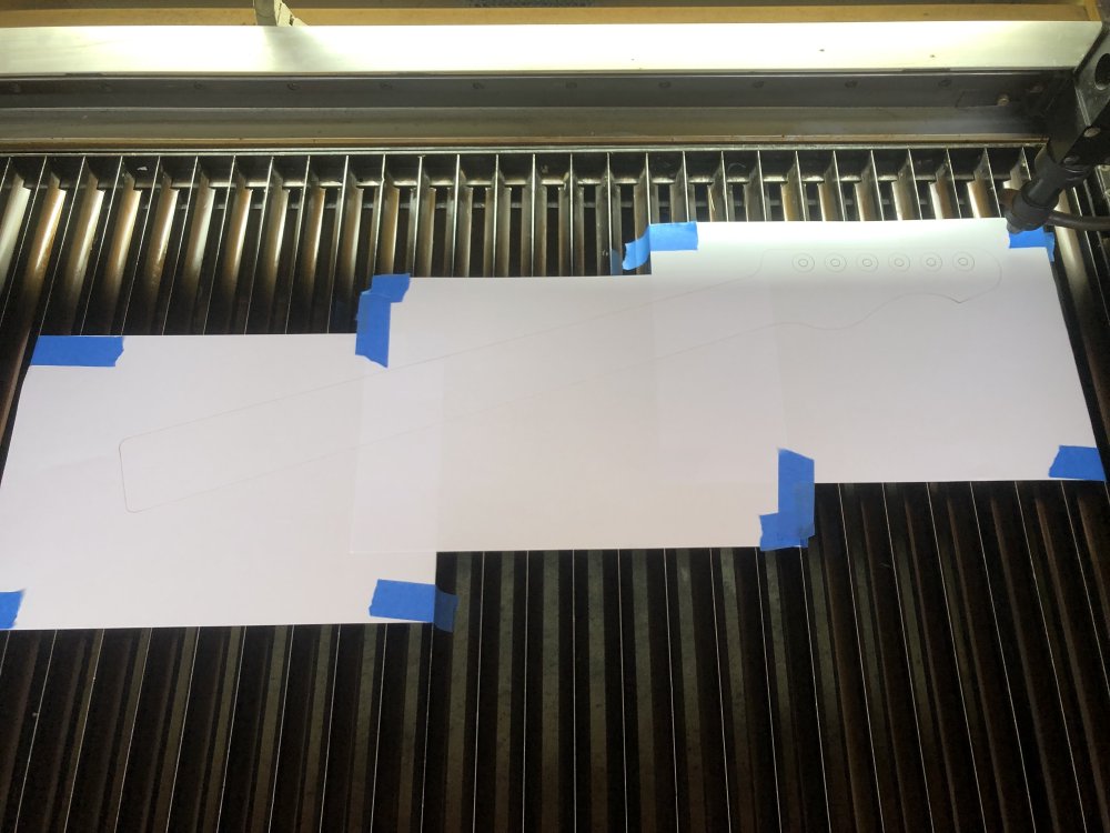 A photo of three sheets of A4 paper stuck to a metal platform (the bed of the laser-cutter) with masking tape, and if one were to look closely you can see the outline of a guitar neck running across the sheets.