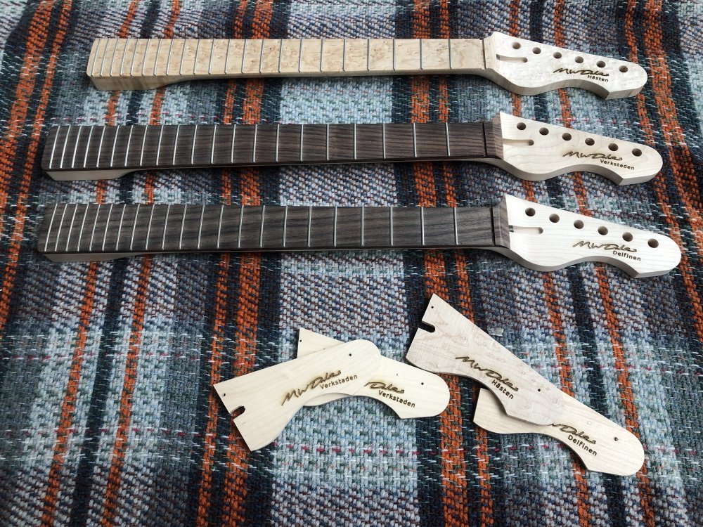 A photo of the three guitar necks and a bunch of headstock test-pieces sat back on the tartan rug, all sporting my signature and a guitar name.