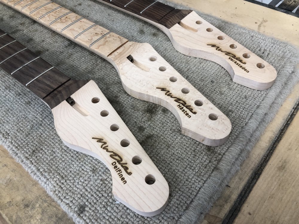 A closeup of the three guitar-neck headstocks with the new logos. You can see some dark marks around where the etching has happened, as sap and wood dust was vapourised in the etching and deposited back down around the logo.