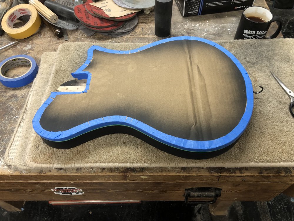 The guitar body from the last image, but now there is a cardboard cutout of the guitar tapeed to the top also, to protect the front from paint.