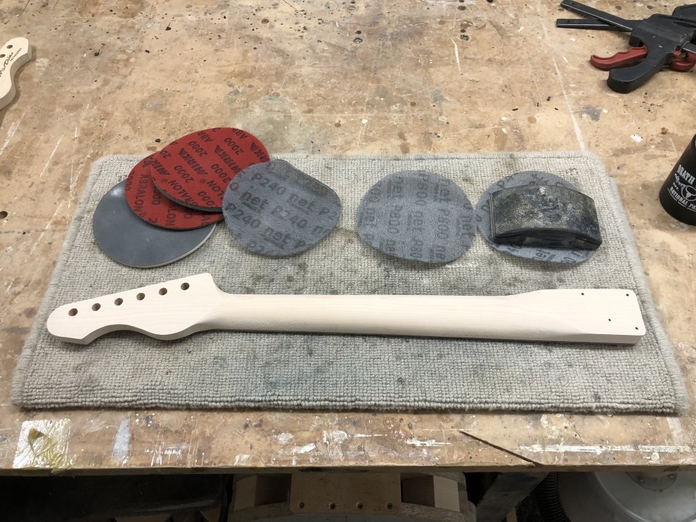 A guitar neck sits face down on the workbench, surrounded by sanding-disks.