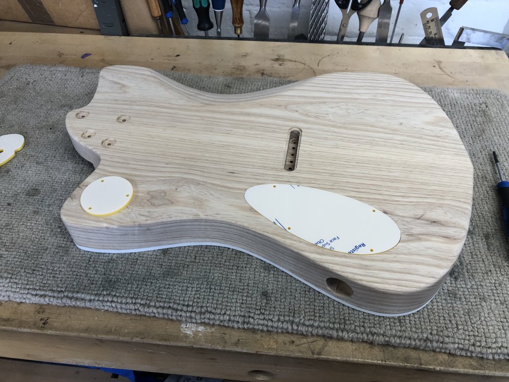 A view of the back of the guitar body again, but now the two caps are placed over their respective cavities. The bigger one sits flush, but the smaller one sits proud.