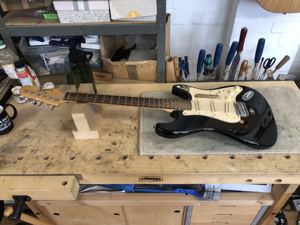 A photo of a black strat clone with white pick-guard sits on the workbench.