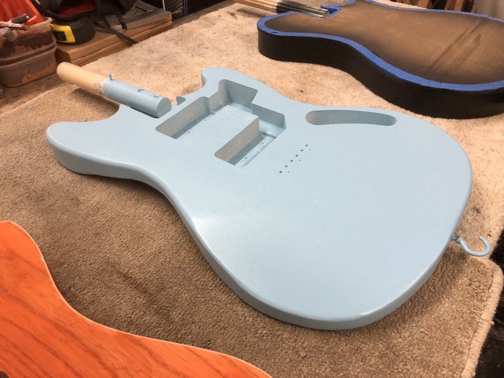 A close up photo of the middle guitar, which is the shape of a Fender Mustang. The body is a pale blue, and if you look closely you can still just see the wood grain patter in the otherwise uniform paint layer.