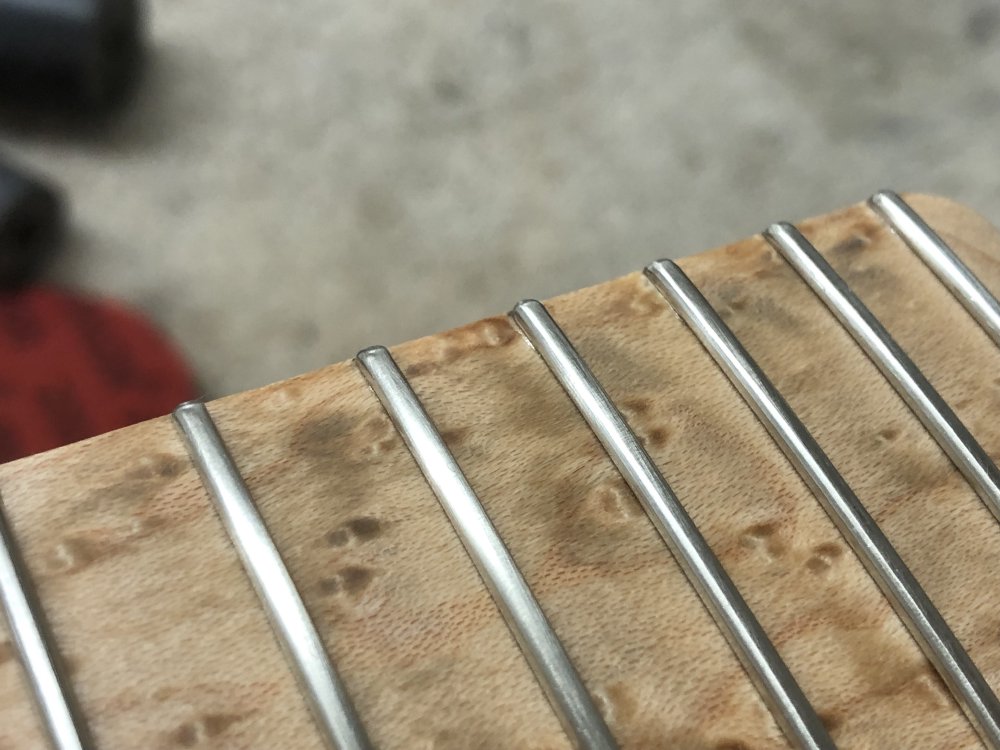 A close up on a birds-eye maple fretboard, and you can just see some lighter areas along the top 5mm of some of the frets.
