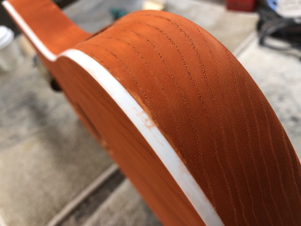 Another close up photo of the same orange-stained wooden body with white plastic binding, only this time looking at the side, and there is a pale orange smudge close to the edge in an otherwise dark orange area.