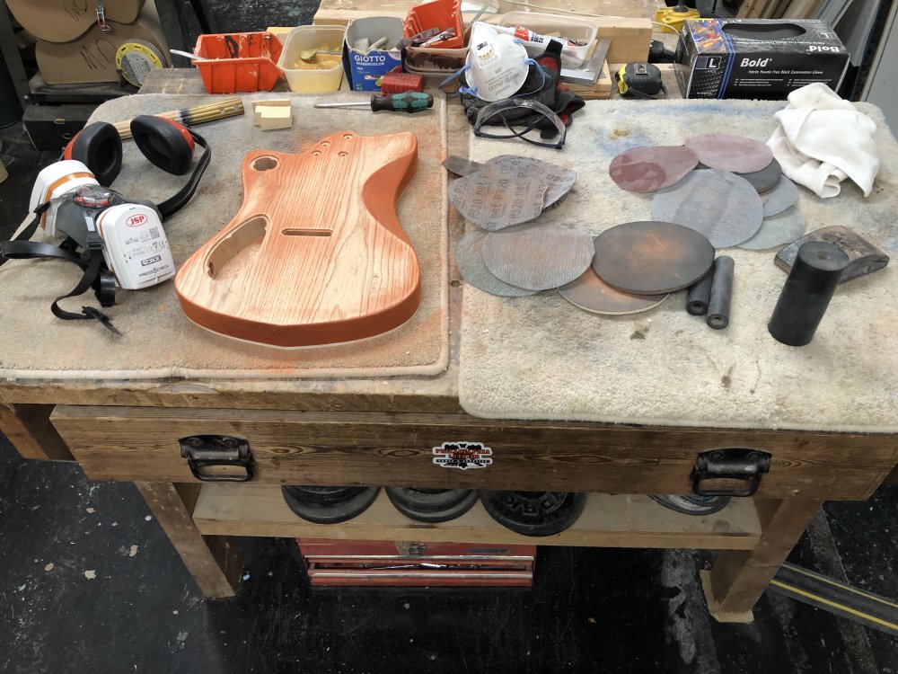 A photo of the guitar body on a workbench surrounded by sanding disks and my respirator mask.