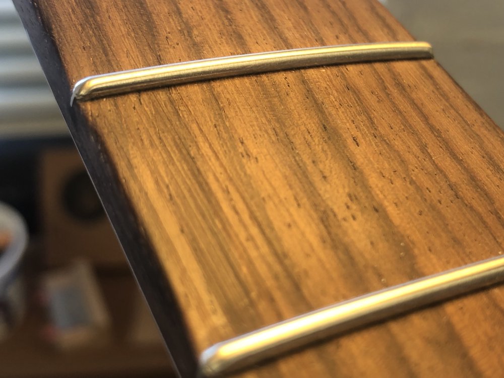 A close-up photo of an area of the fretboard between two frets, and you can see some straight scratch marks running along the length of the neck. The fret-ends are nicely hemispherical though, so it's not all bad.