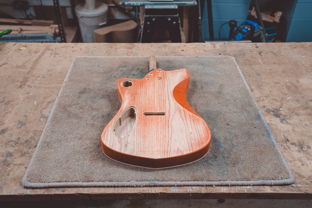 A photo of the same guitar body as the previous photo, but this time face down, showing that it was once stained orange but has since been sanded back to mostly unstained wood.
