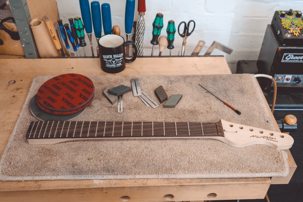 Another photo of the neck on the workbench, this time just the small file remains, and then additionally there are high-grit sanding pads, metal fret-board protectors, and fret-polishing rubbers.