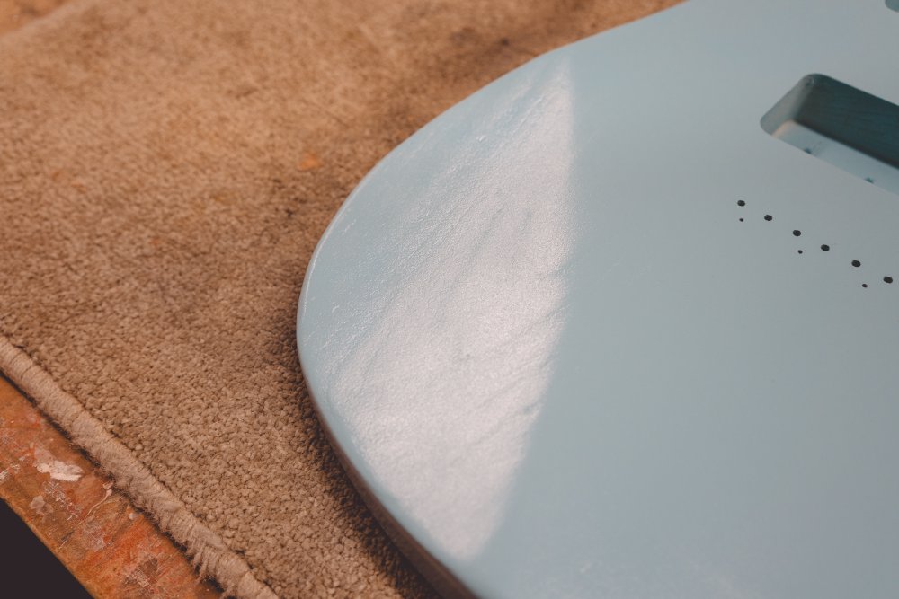 A close-up photo of the light blue painted body, catching the light in the paint to show that you can still see the grain of the wood in the painted finish.