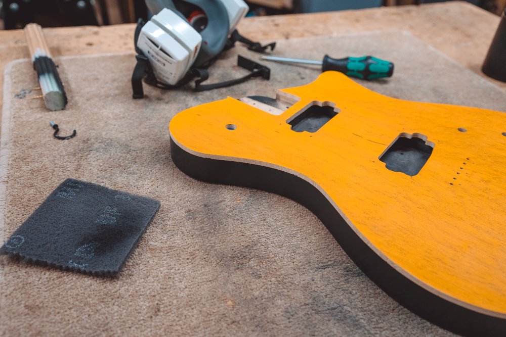 A photo of a single-cut style guitar body sat on the workbench. The top is yellow stained maple, with 5mm of the side next to the top being natural maple, and then the rest of the side being black paint.