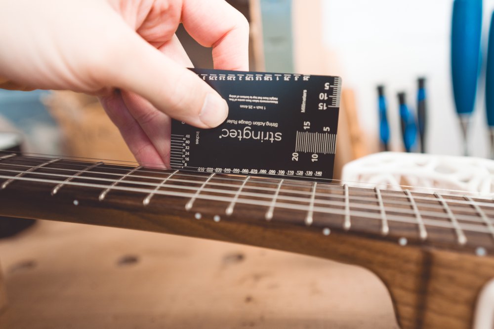 A close-up photo of a measuring card being held at the 12th fret on the neck of the unusual guitar.