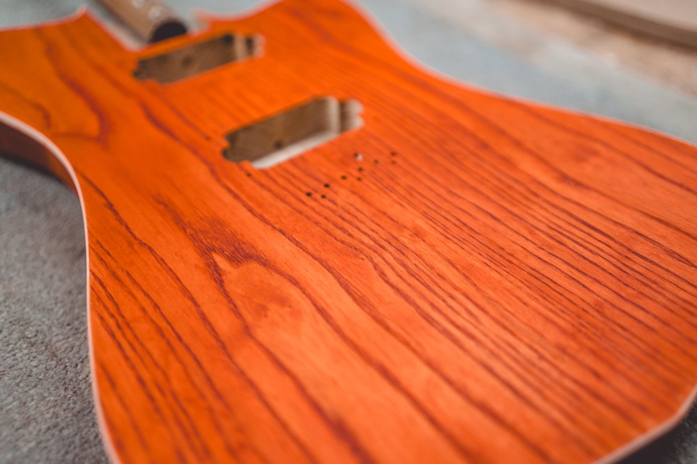 A close-up photo of the front of the orange-stained guitar body showing how the grain stripes are now much darker than the surrounding wood.