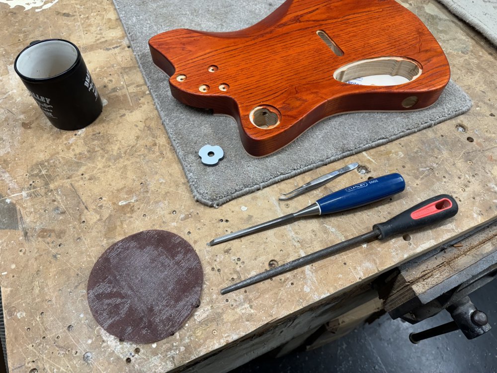 A photo of the same scene as before, but now there is a chisel, a rasp, a pair of tweezers, and a sanding disk sat next to the body.
