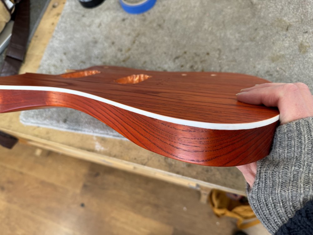 An after shot of the guitar body, showing a clean white line now exists between the face of the guitar and the side of the body, both of which are stained a dark orange.