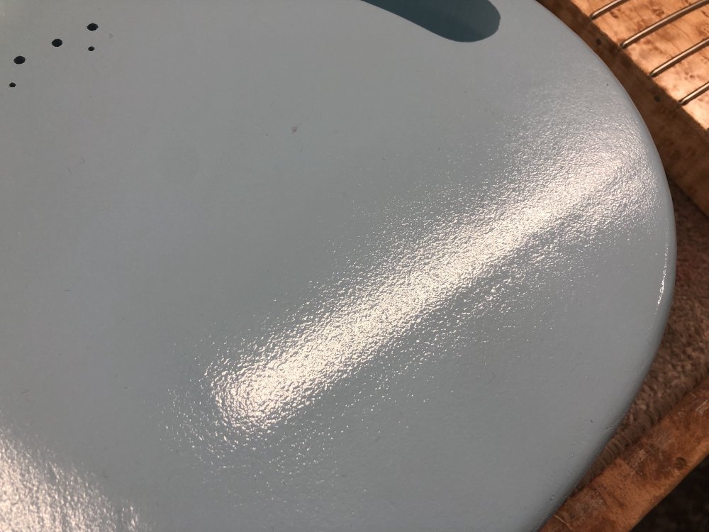 A close up photo of one of the flat areas of the guitar body, with light reflecting off the paint, and you can see the final finish has a very speckled texture to it.