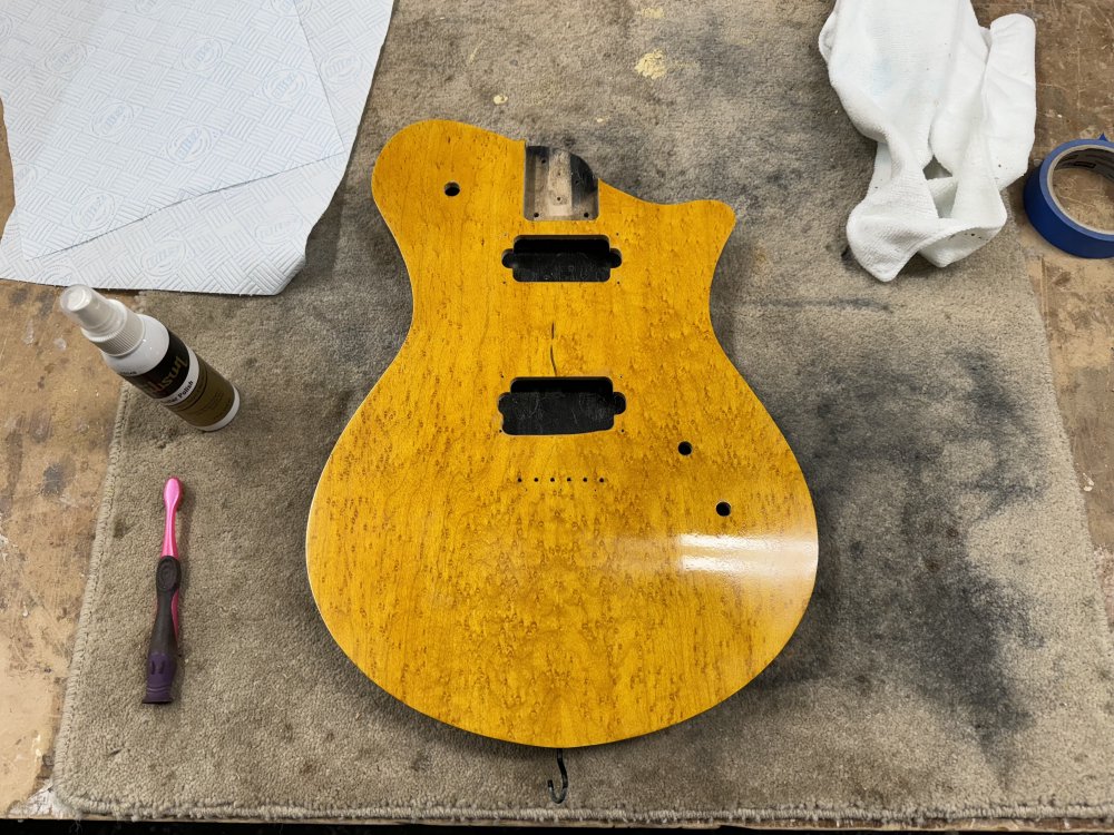 A photo of the guitar body on the workbench, yellow side up. Next to it is a bottle of polish liquid, an old toothbrush, and a microfibre cloth.
