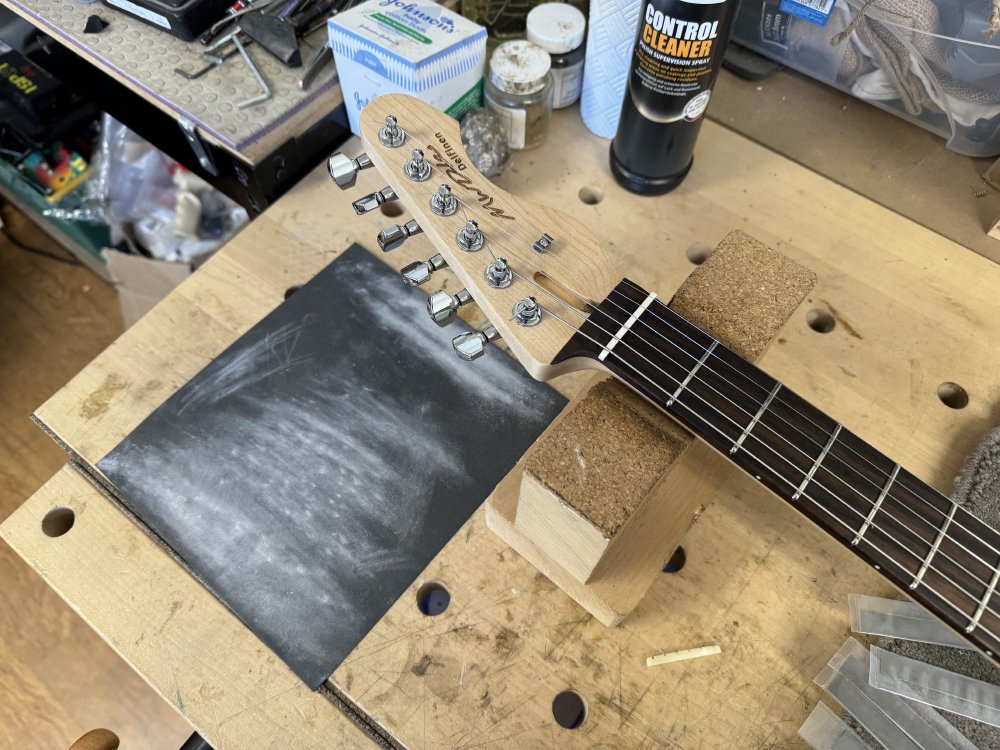 A close-up photo of the top of the guitar neck, showing the new nut in place. Behind it you can see some sandpaper that is covered in white dust from where the nut was sanded down to size.