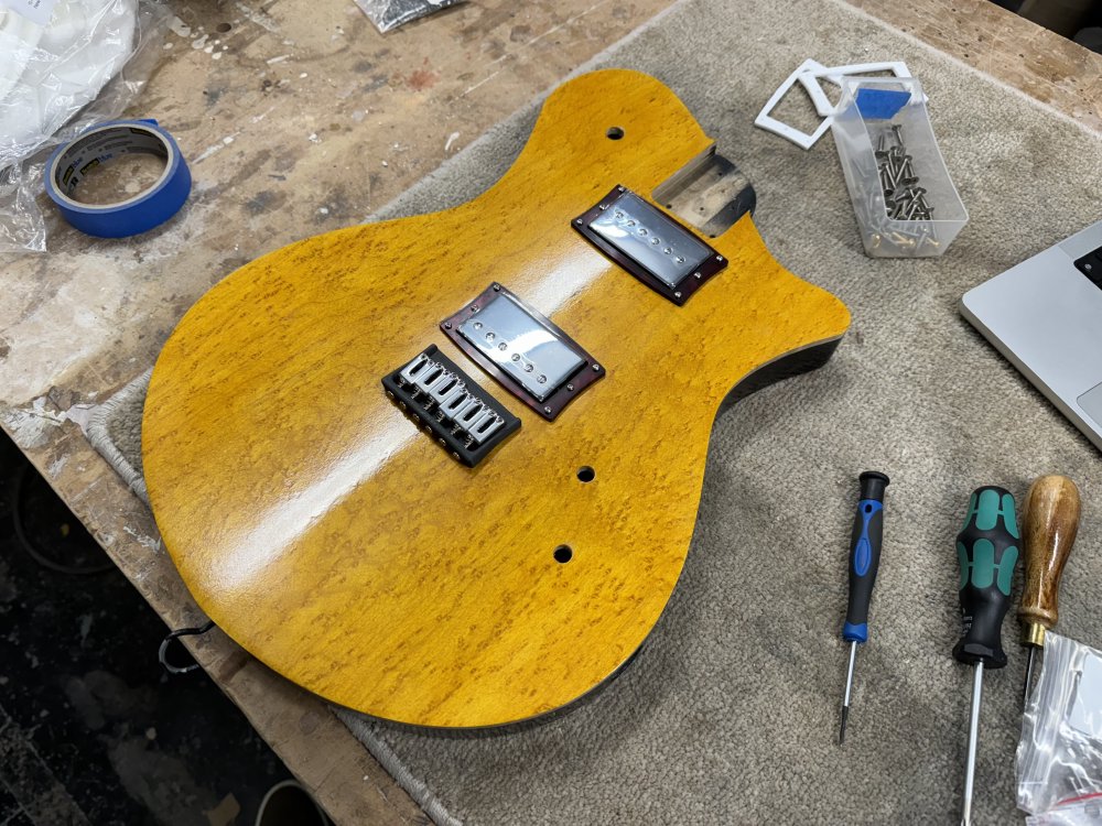 A photo of the yellow-capped guitar body with both pickups and a hardtail bridge in place. The bridge has chrome saddles and a dark grey bridge-plate.