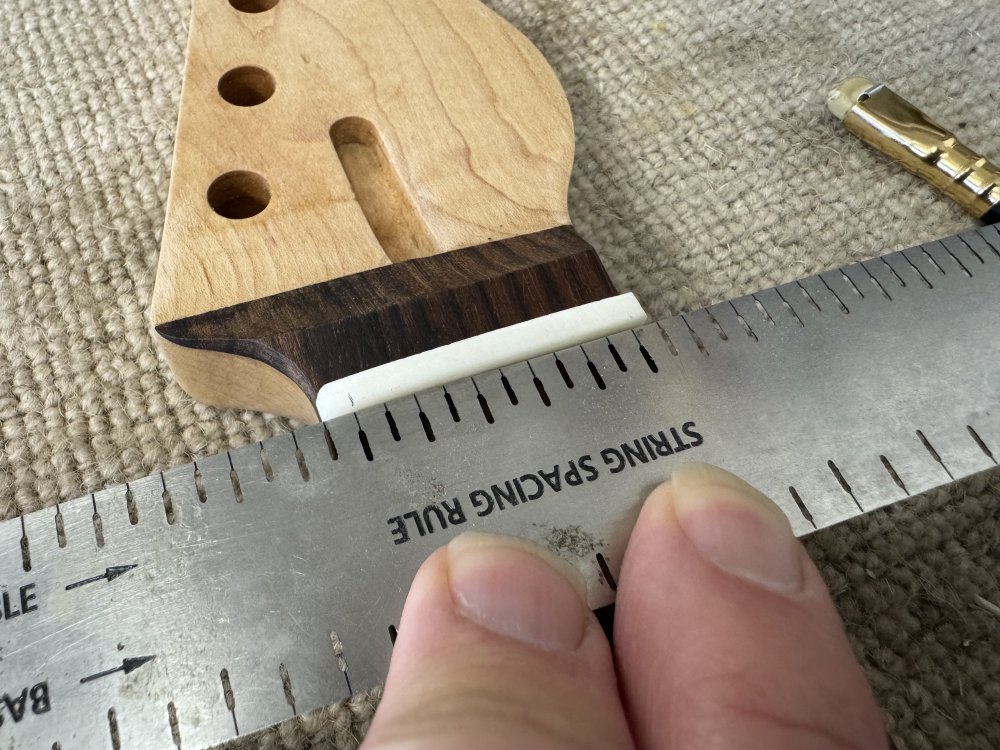 A close-up photo of the nut in the neck, with two pencil marks on the top, each about 3mm from the either edge, and the string spacing ruler pressed up against it so that there are six slots in the ruler that match the string spacing for this neck.