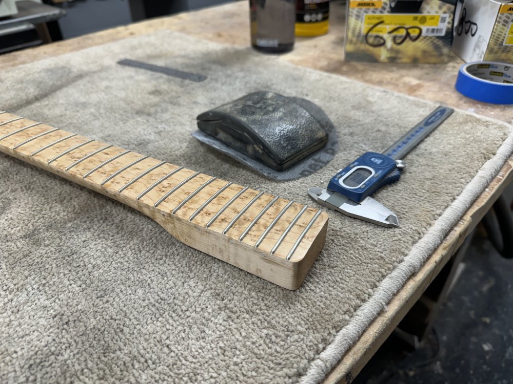A photo of the heel end of the same neck, and you can see that the finish has been sanded away from the sides of this end of the neck. Next to the neck sits a set of measuring callipers.