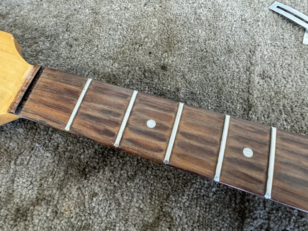 A view of a well worn rosewood fretboard, showing where over the years the strings have been pressed down.