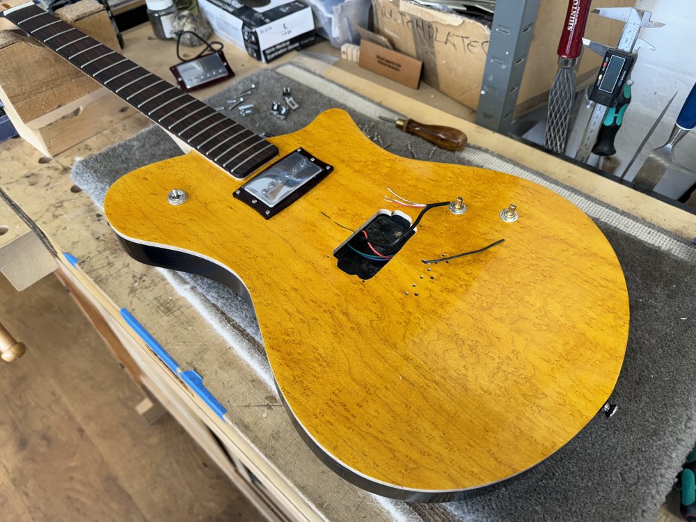 Another photo of the guitar on the workbench, only now the strings and bridge have been removed, along with the bridge pickup, and you can see wires poking up through the hole where the pickup should be.