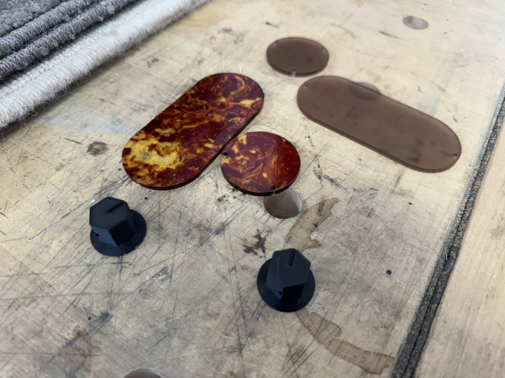 A photo of two black plastic control knobs (for the volume and tone) and two pairs of laser cut acrylic covers, one in frosted orange and the other in orange/red translucent marble effect.