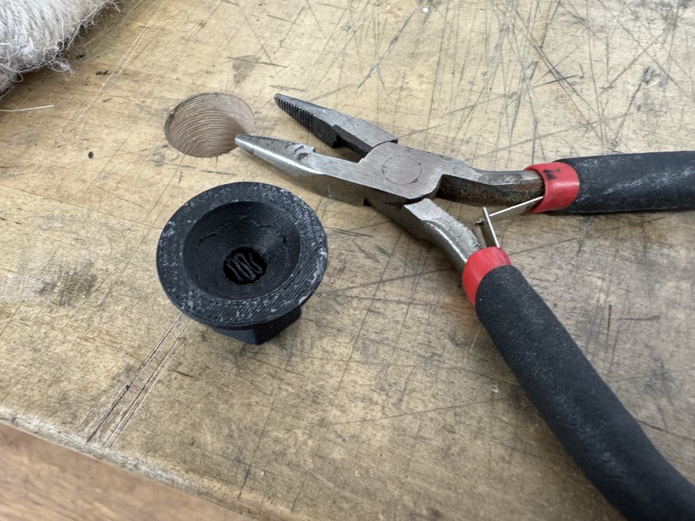 A photo showing that some of the support material has been removed from the knob, which is sat next to a set of pliers on the workbench.