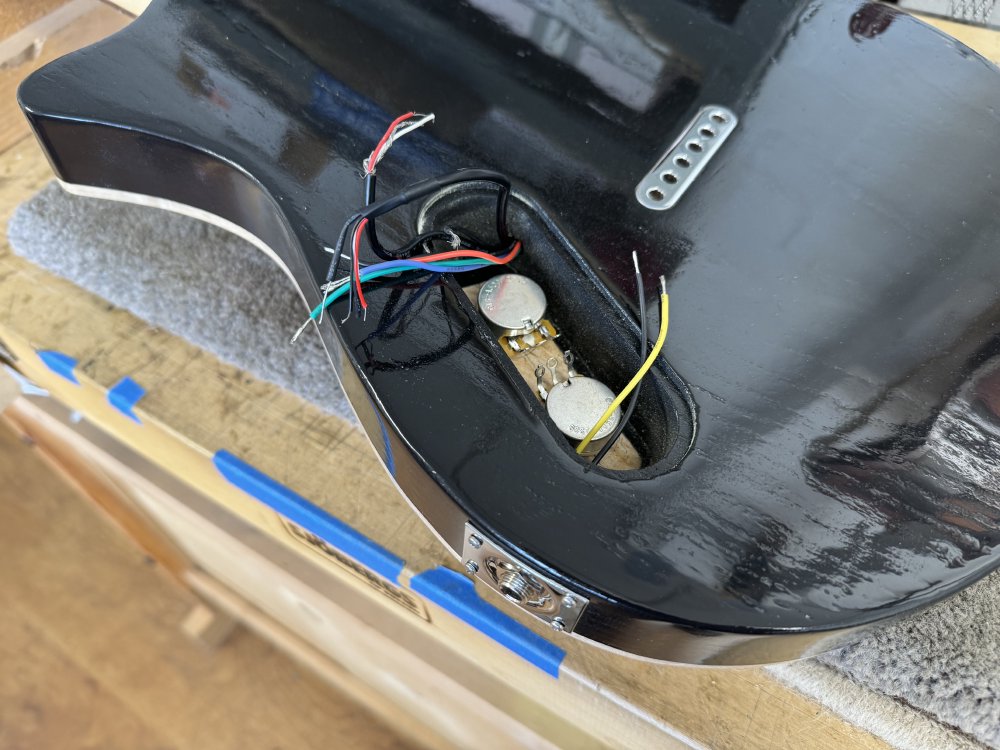 A photo of the back of the guitar body, showing a lozange shaped cavity into which some wires are poking, and the back of the two potentiomenters can be seen. The cavity is not much bigger than the space required for the two pots.