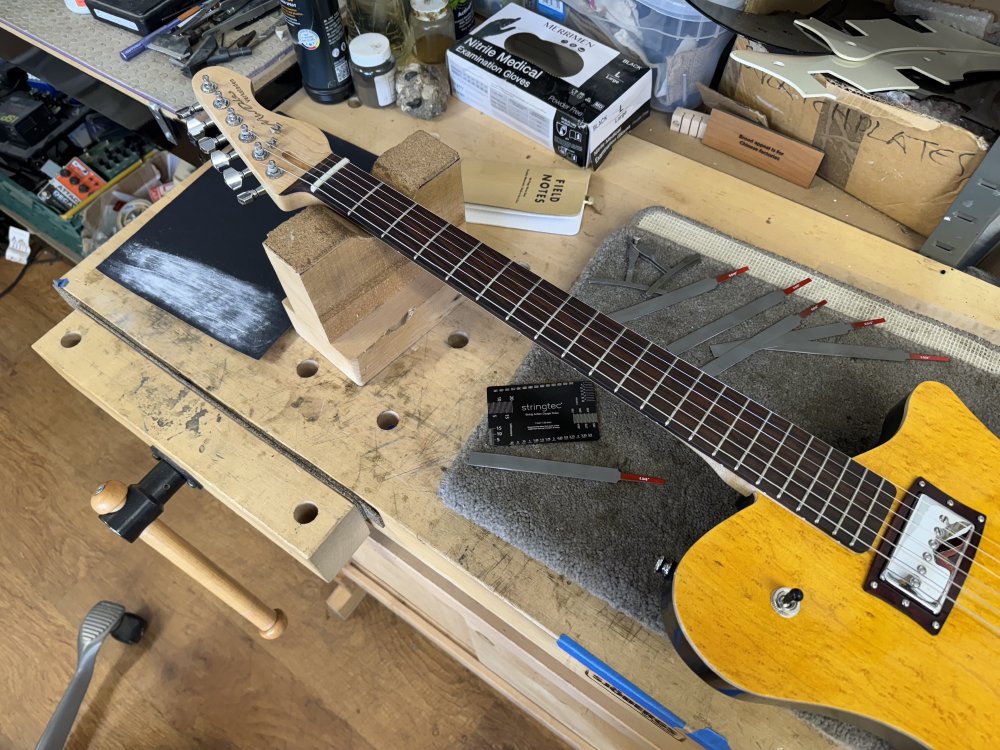 A photo of the completed guitar sat on the workbench, next to which sit a variety of measuring and filing tools ready for doing the final set up.