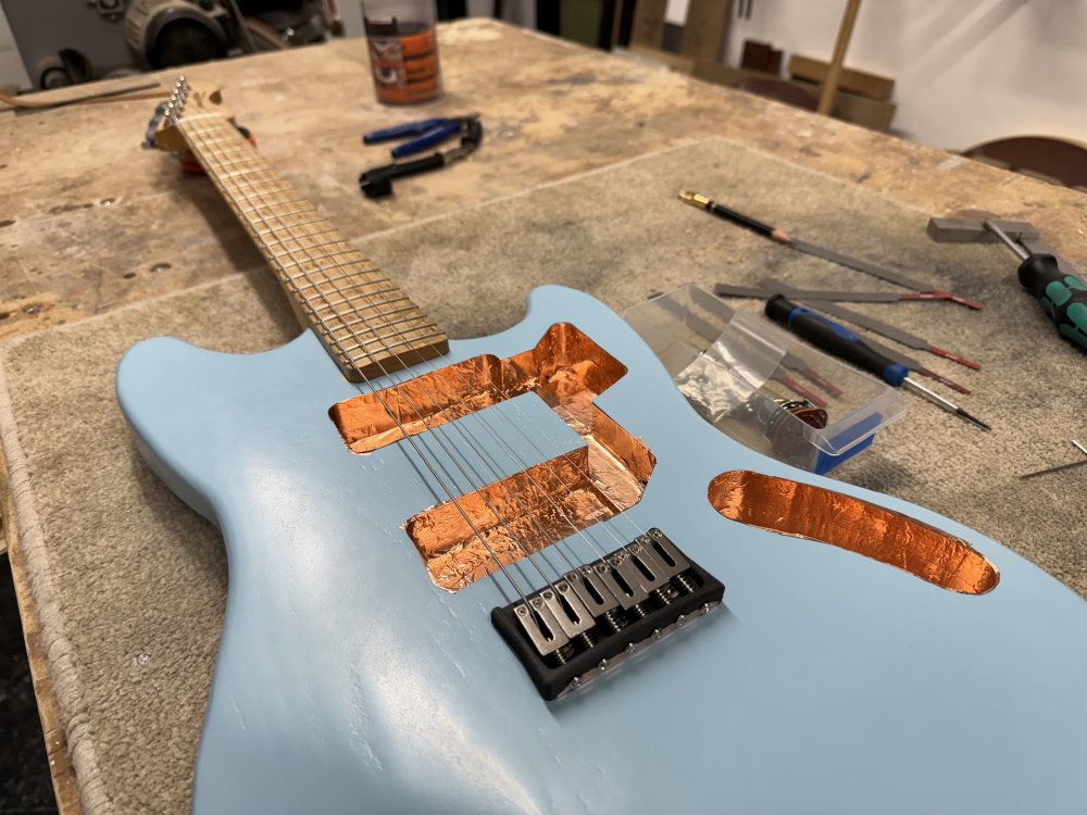 A photo of the guitar on the workbench again, only now despite the lack of pick-guard and electronics still, there are strings installed.