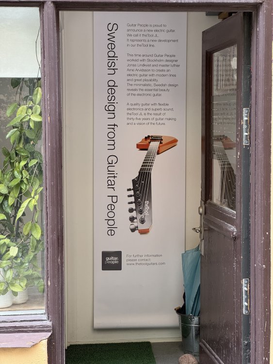 A photo taken of a doorway into a building, showing a door height poster in the little hallway titled 'Swedish design from the Guitar People' and a picture of an electric guitar with a minimal headstock.