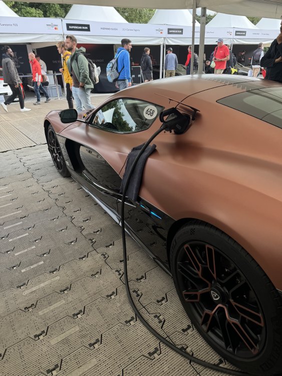 A photo of a bronze coloured hypercar, into which a charging cable has been plugged. The thick and heavy charging cable rests on one of the creases in the bodywork, and so a small towel has been placed between the bodywork panel and the charging cable to prevent it making marks on the paint.